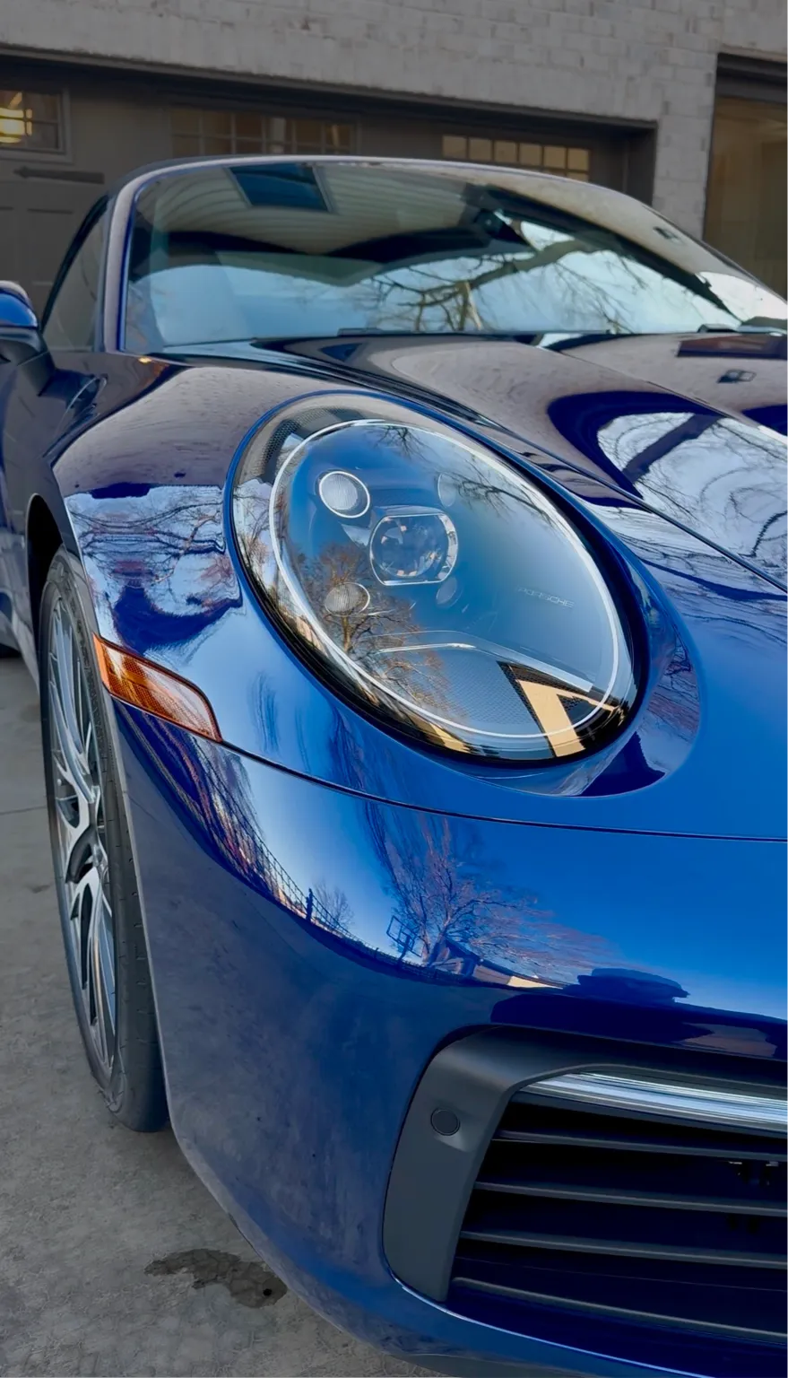 Close-up of the front left headlight and hood of a shiny blue sports car parked on a driveway.
