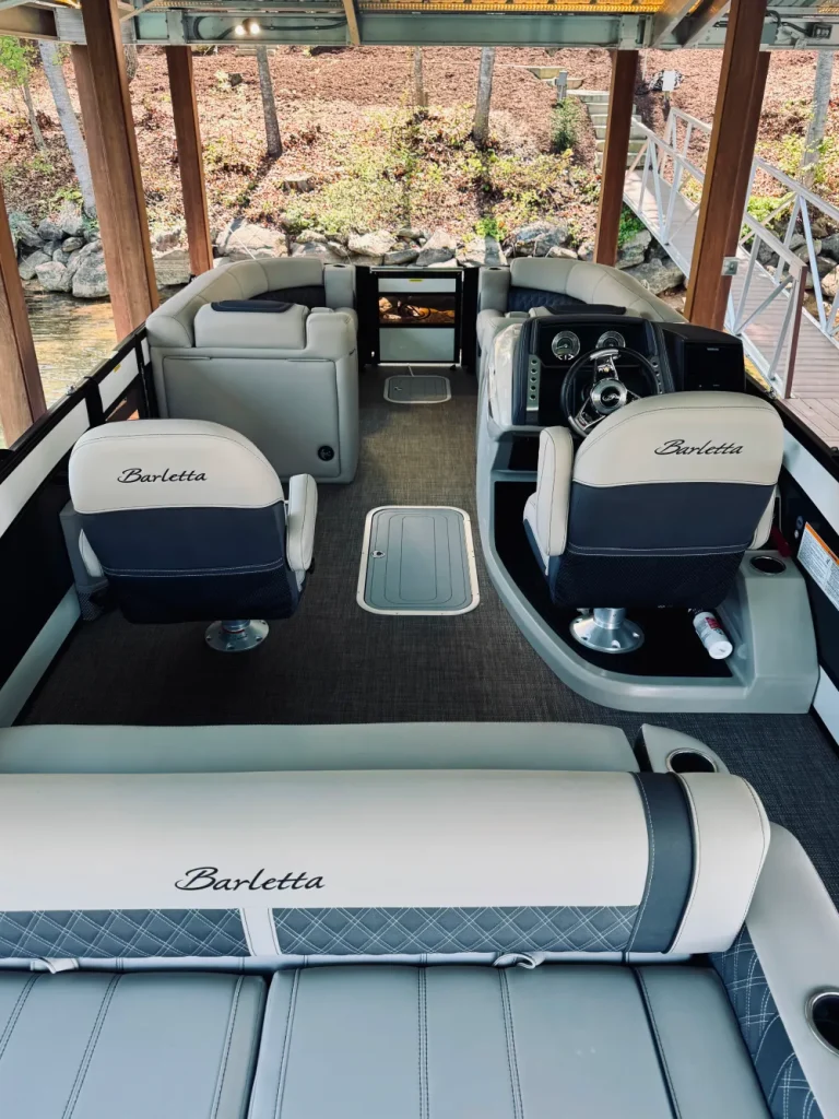 gallery-16 Barletta pontoon boat interior with seats, helm, and dock in the background, under a covered structure.