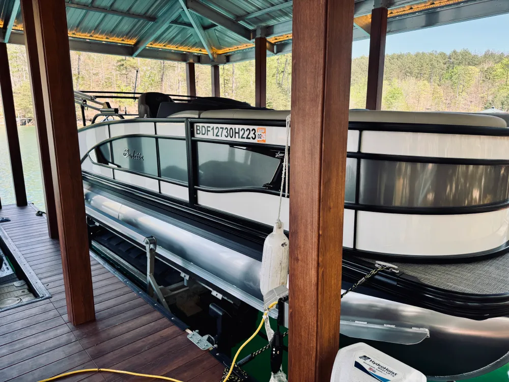 gallery-18 A white pontoon boat is docked under a covered wooden boathouse on a lake.
