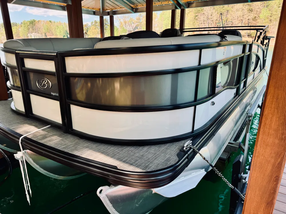 gallery-19 A white and black pontoon boat is docked under a wooden shelter on a green lake.