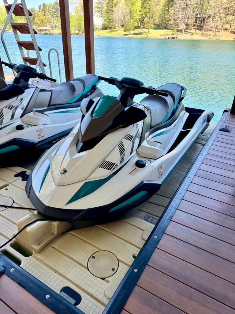 gallery-2 A white and teal jet ski is parked on a dock next to a lake on a sunny day.