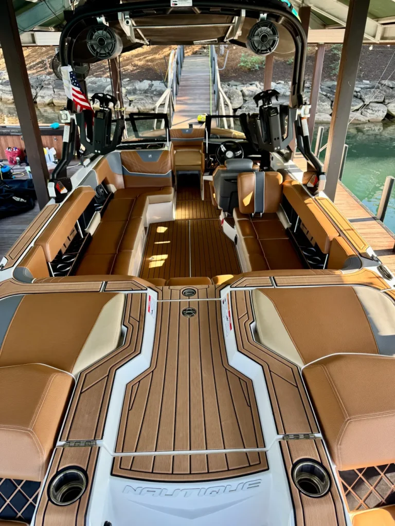 gallery-26 Luxury Nautique wake boat with tan seating, teak flooring, and open deck docked at a pier.
