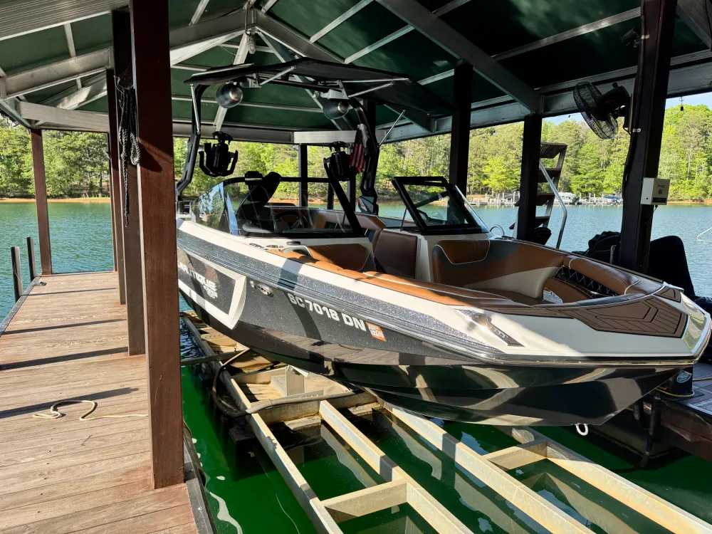 gallery-28 A black and white speedboat docked under a covered boathouse on a sunny lake with trees in the background.