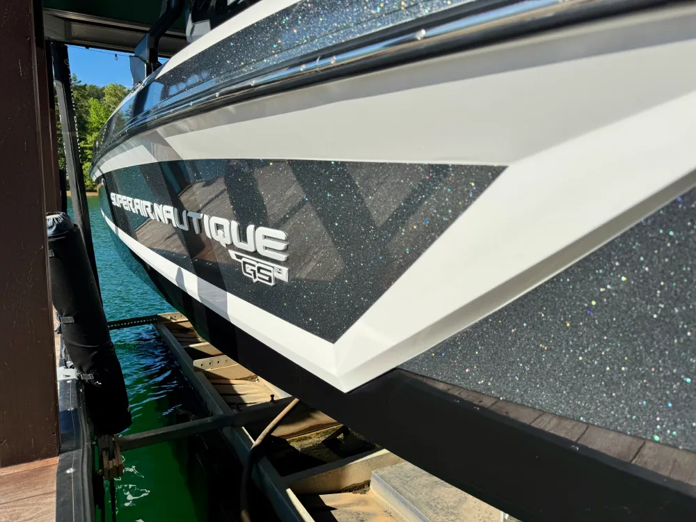 gallery-30 Close-up of a black and white Super Air Nautique GS3 boat on a lift by the water.