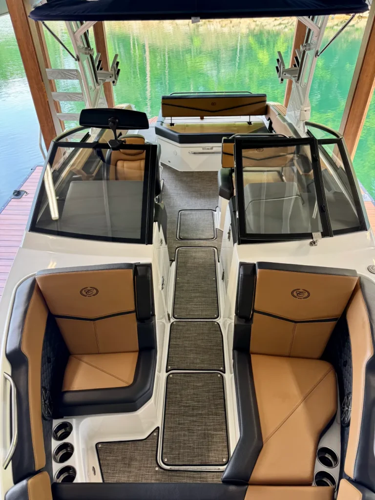 gallery-32 Luxury boat interior with tan and black seats, a walkway, cup holders, and water visible in the background.