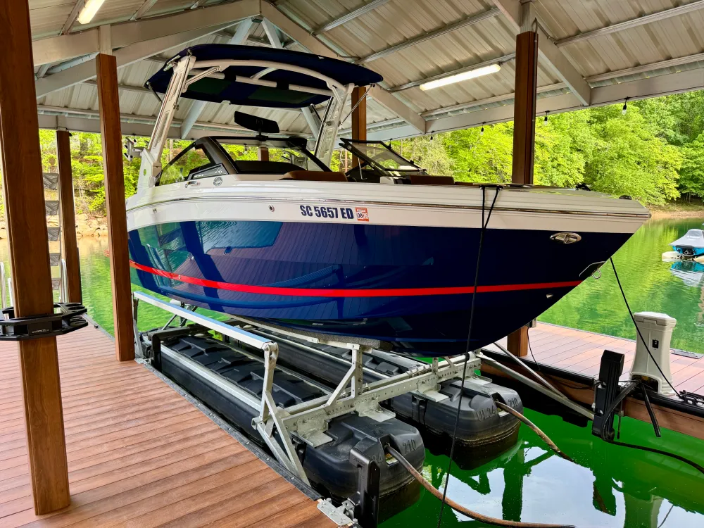 gallery-35 A blue and white boat sits on a lift in a covered dock over green water, surrounded by trees.