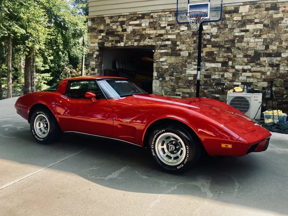 gallery-39 A classic red sports car parked on a driveway, with a stone wall and basketball hoop in the background.