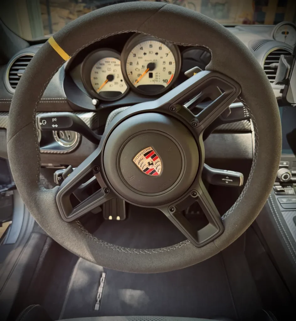 gallery-47 Close-up of a Porsche sports car steering wheel and dashboard, with white gauges and sporty interior.