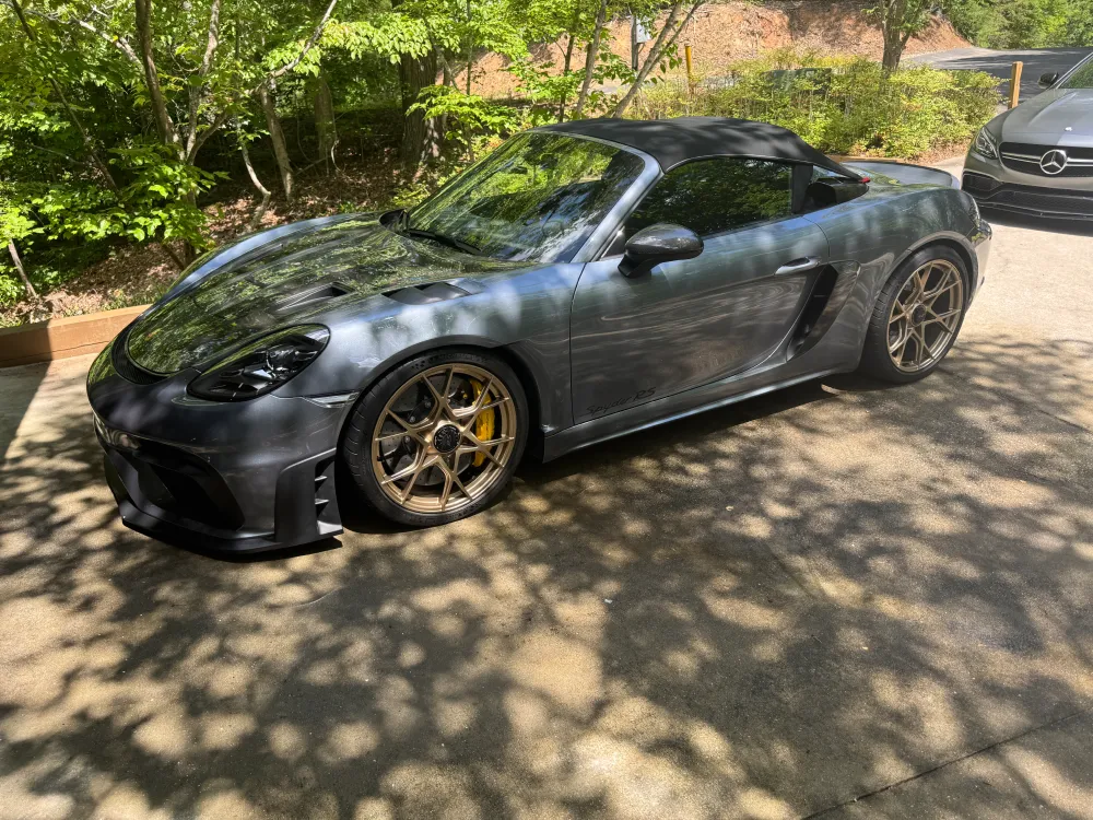 gallery-48 Gray convertible sports car parked on a driveway with trees casting shadows around it.