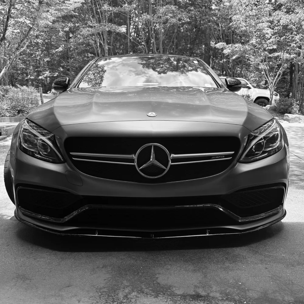 gallery-49 Front view of a Mercedes-Benz car parked outdoors, surrounded by trees, in black and white.