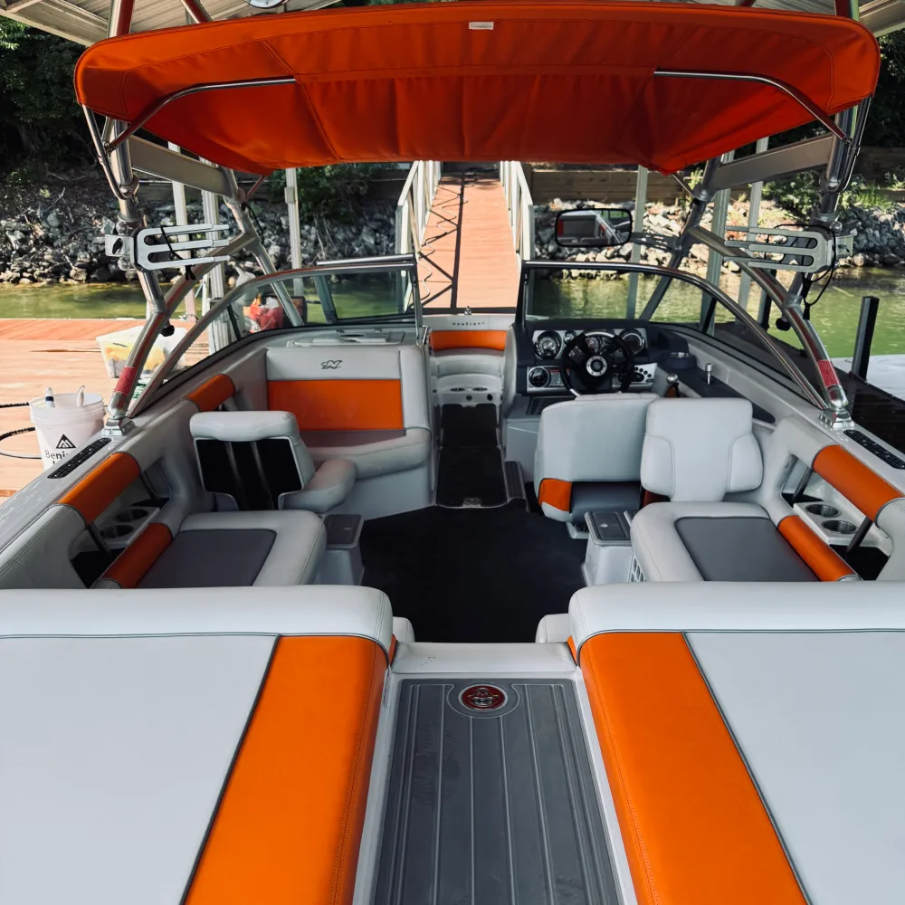 gallery-51 Wake boat with orange and gray seats docked at a pier on a lake, seen from the back of the boat.