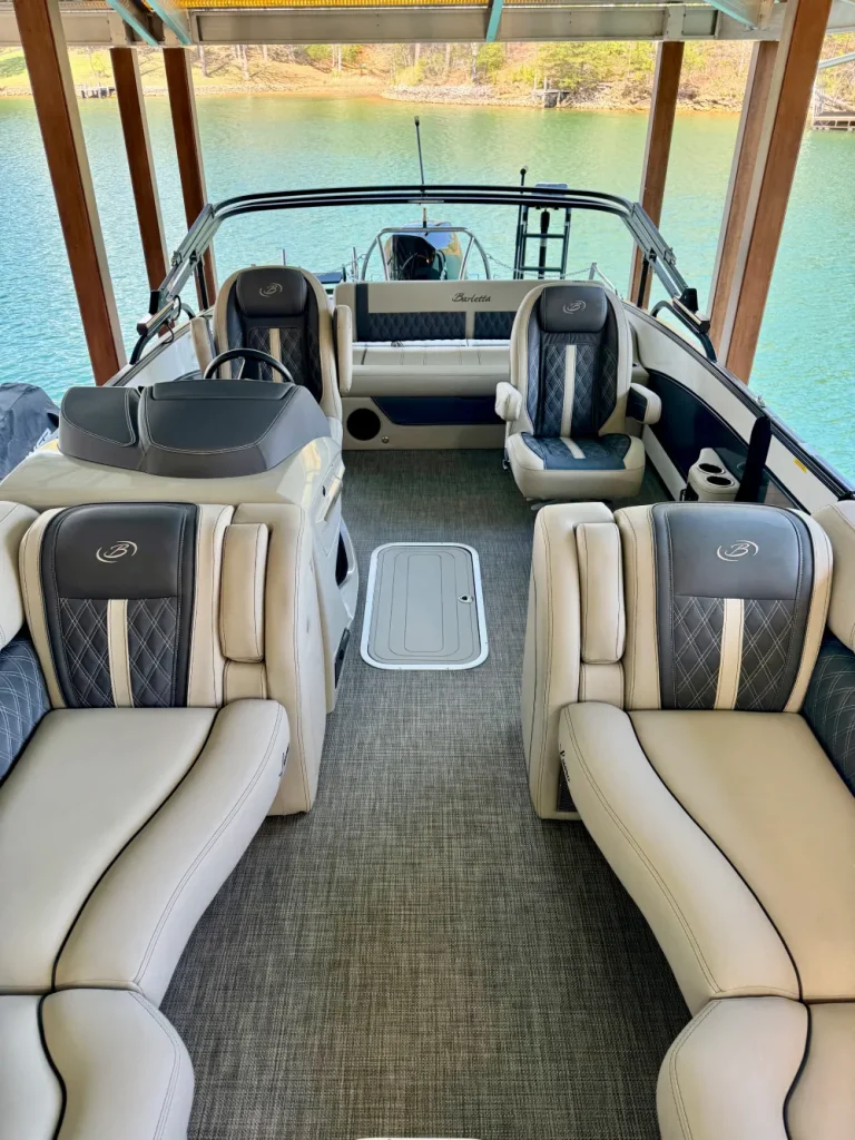 gallery-6 Pontoon boat interior with plush seating, gray carpet, and lake view in background under a covered dock.