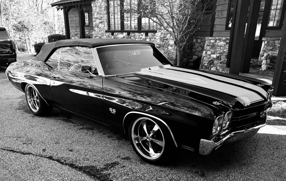 gallery-8 Black and white photo of a classic convertible muscle car parked on a street in front of a stone house.