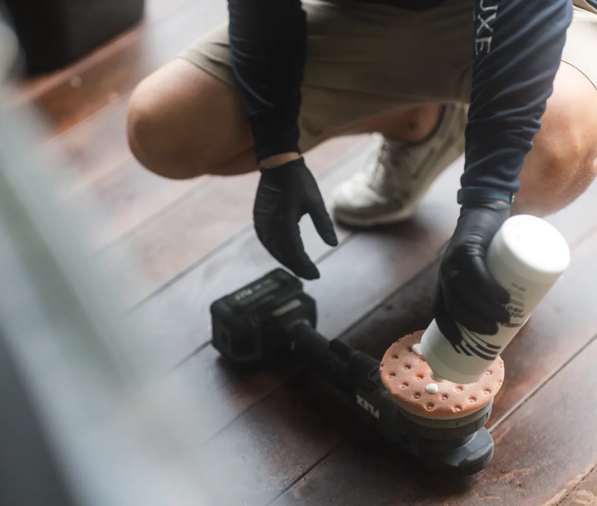 Person in gloves applies polishing cream to a power buffer on a wooden floor.