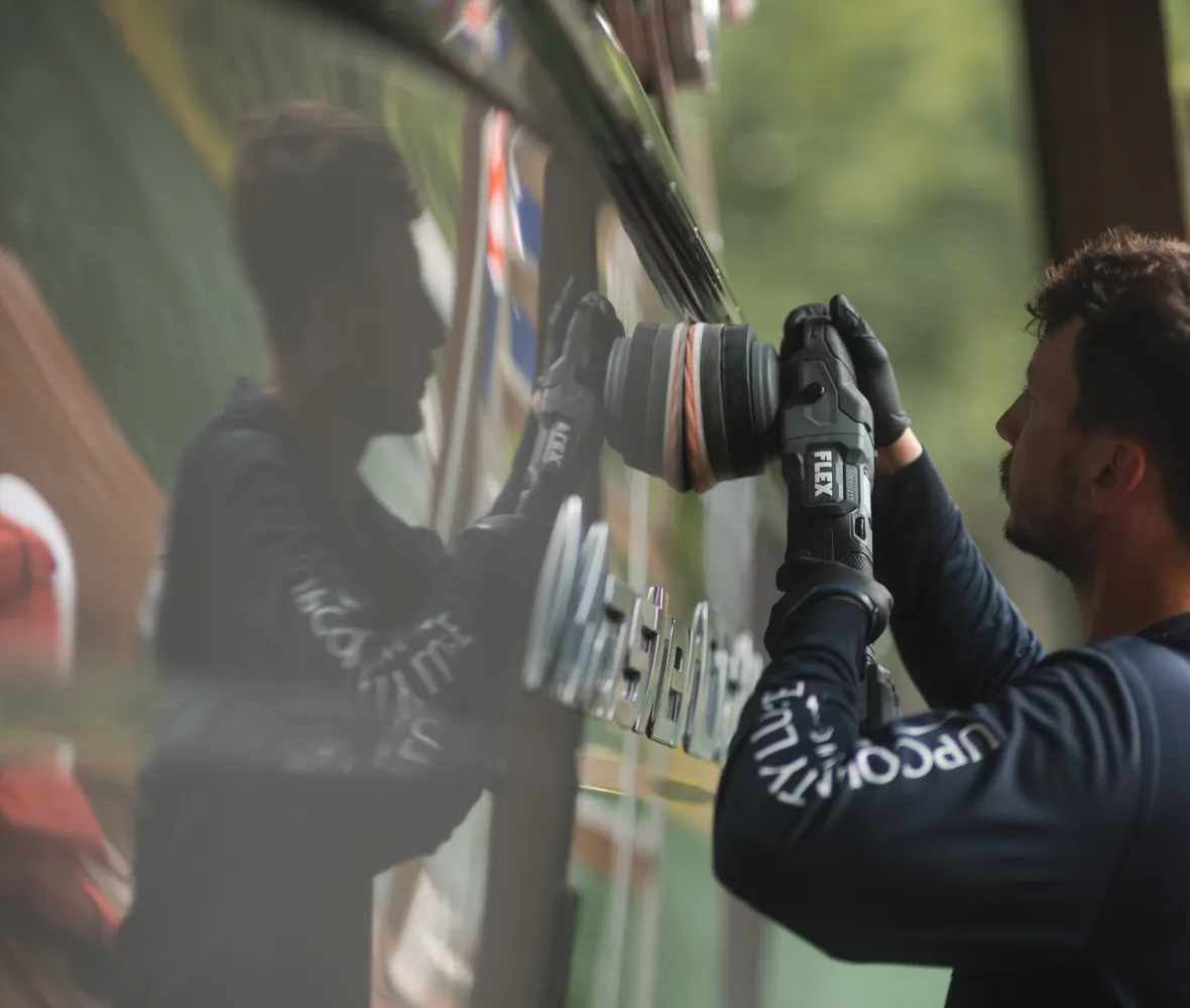 Person wearing gloves polishing a reflective vehicle surface, with their reflection visible.
